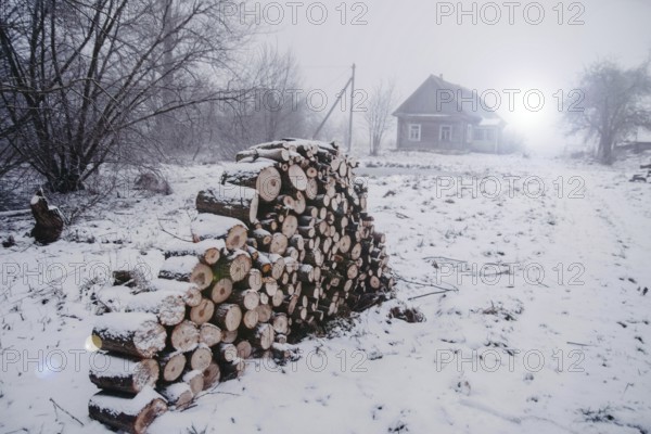 Snowy landscape with a cabin and stacked firewood, depicting a cold rural winter scene