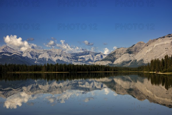 The Canadian Rockies and bright blue sky are reflected in a lake near Canmore, Alberta, Canada, North America