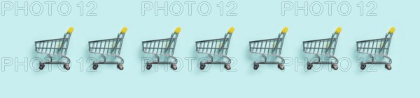 Shopping cart in row on blue background. Minimalism style. Toy trolley for supermarket. Top view or flat lay. Sale, discount, shopaholism concept. Consumer society trend