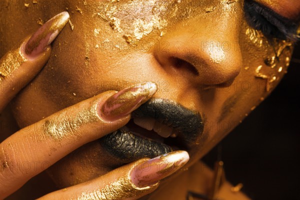 Beauty fashion model girl with golden make up and body on black background. Golden body art. The golden face of a beautiful lady is touching. Artistic portrait