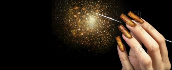 Hand with gold manicure and a brush on a black background covered with sparkles. Nail design. Extended nails