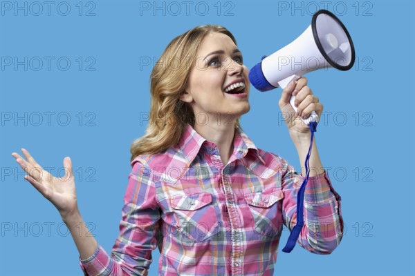 Excited young woman talking into megaphone on color background. Holiday sales