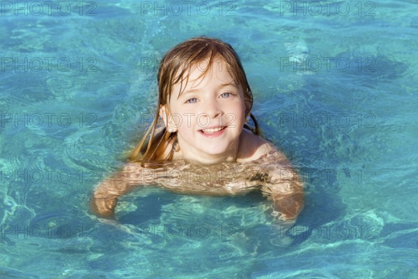Blond little girl swimming on turquoise beach in Ibiza