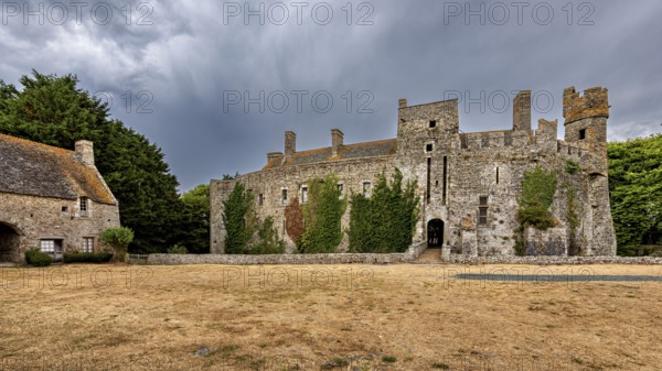 Expansive view of a castle with ivy and a cloudy sky, Pirou Castle in Normandy, France
