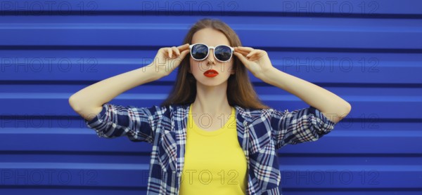 Portrait of modern stylish young woman in white glasses, casual clothing posing on blue wall background