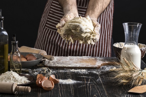 A handful of flour with egg on a rustic kitchen. Against the background of men's hands knead the dough. Ingredients for cooking flour products or dough bread, muffins, pie, pizza dough . Copy space