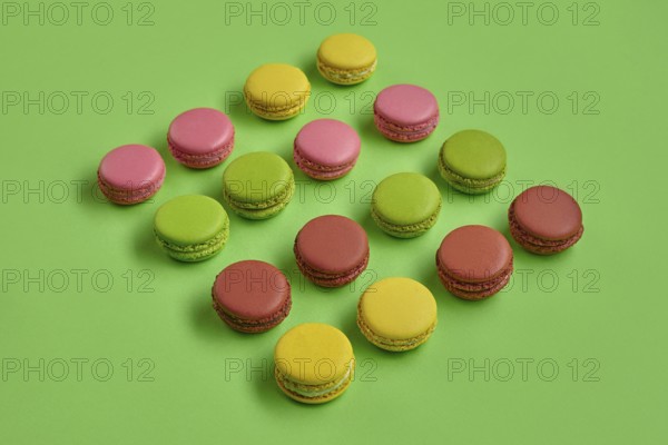 Top view of a yummy macarons or macaroons, sweet meringue-based confection with a ganache, buttercream or jam filling sandwiched between two such cookies. Tasty biscuits on green background. Close-up, copy space