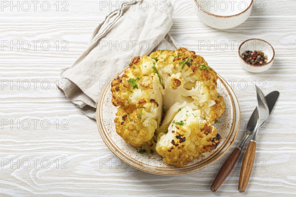 Whole roasted head of cauliflower with olive oil on plate on white wooden rustic table top view with cutlery. Vegetarian dish, space for text, food photography, food photography