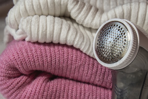 Anti-pilling razor. Device for shaving clothes. Anti-Plush fabric Shaver. Electric portable sweater pill defuzzer Lint remover from pink acrylic or wool sweater. Electric device fabric shaver after cleaning and collected fluff lint. Closeup Pilled sweater. Old used clothes with pilling