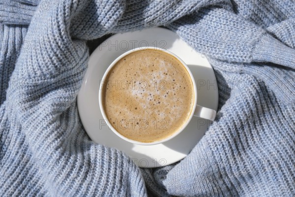 White cup of morning coffee on blue sweater background. Cozy home autumn concept. Aesthetics blog lifestyle. Still life concept. Cappuccino or latte hot drink. Top view flat lay
