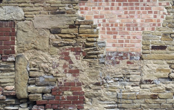 A large old wall made of mixed bricks and stone with many jumbled patched and uneven repairs