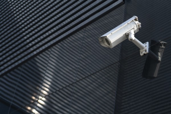 Photo of Modern CCTV camera on a wall. A blurred night cityscape background. Concept of surveillance and monitoring. Toned image double exposure mock up