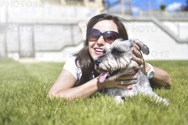 Pretty adult caucasian happy woman resting in the park on a sunny day with her beloved dog. Female lay on the grass smiling and looking at the camera