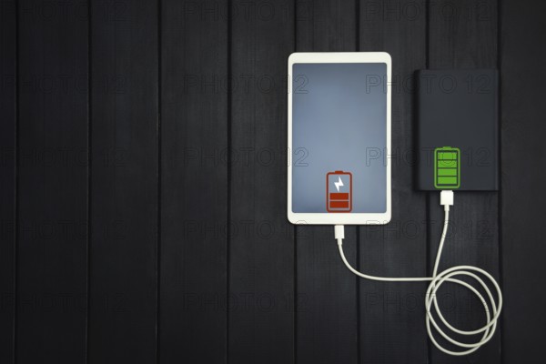 Power bank loads tablet PC, smartphone, isolated on wooden background. charging concept. free copyspace