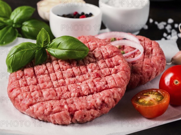 Close up view of two raw meat steak cutlets for burger with vegetables, spices and fresh basil. Making homemade burger