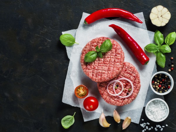 Two raw beef meat steak cutlets for burger with spices and vegetables on black concrete background. Making homemade burger concept. Top view or flat lay. Copy space
