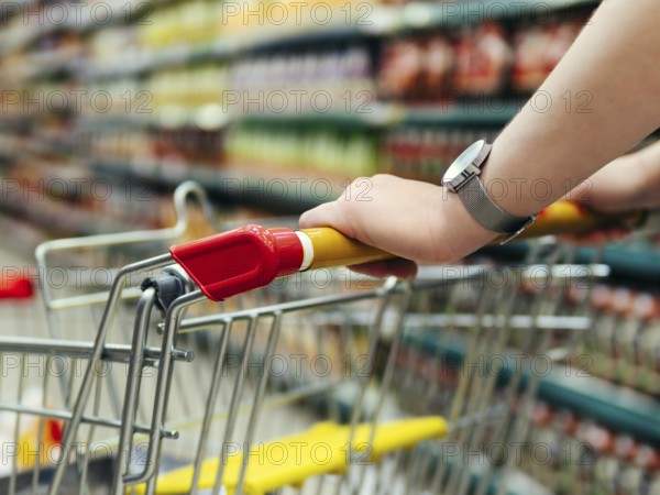 Shopping cart in supermarket. Woman hands hold shopping trolley in supermarket aisle