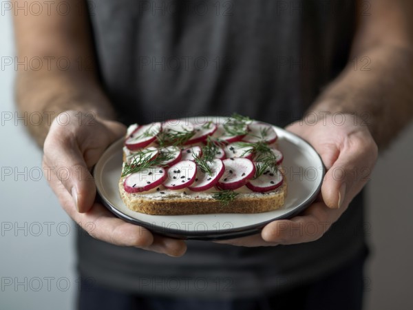 Hands takes plate with vegan sandwich. Healthy appetiezer - whole wheat bread toast with plant-based soft cheese, radish, dill and black sesame