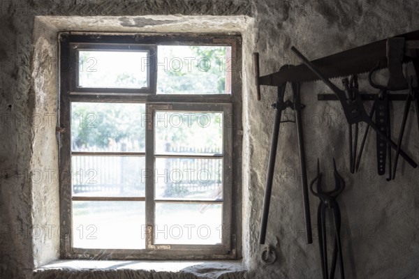 Aged window and blacksmith tools hanging on an old wall, in the interior of a German house