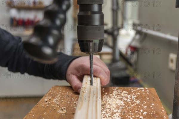 Carpenter drills a hole in the wood with an electric drill - close-up