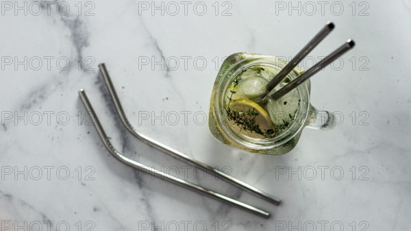 Metal drinking straws and cold drink in glass mason jar on white marble background. Top view or flat lay. Copy space for text or design. Recyclable straws, zero waste concept. Banner