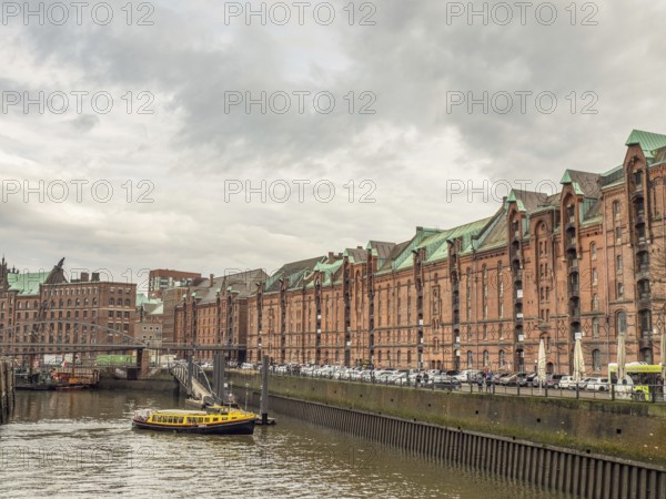 Yellow boat on a river next to historic brick-red buildings and a metal bridge under a cloudy sky, Hamburg, Germany