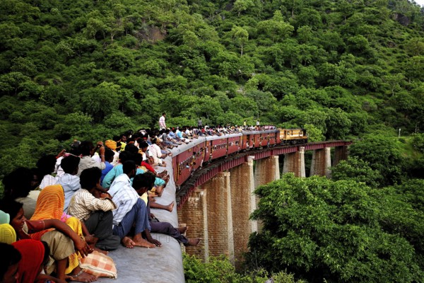 Commuters sitting on roof of train on bridge, Kamali Ghat, Rajasthan, India
