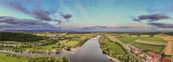 The view shows the wide flowing landscape with the Danube (Lower Bavaria) in the foreground. The gentle hills and meadows glow in the soft colours of the sunset