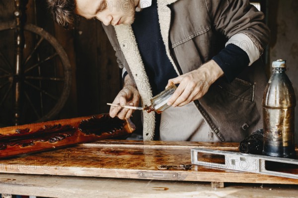 Man applying varnish to wood with precision in a rustic workshop
