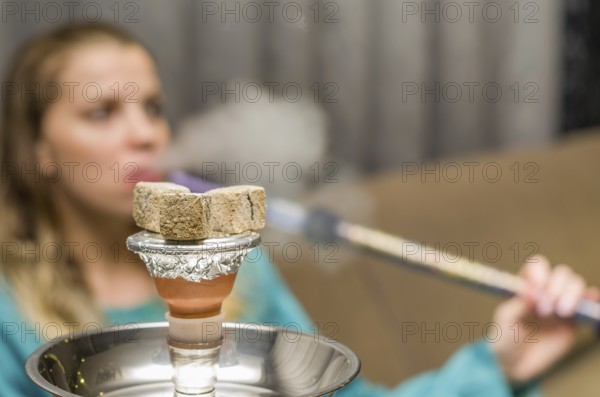 Woman in background blurred, smoking traditional Hookah (Narguile, Shisha, Chicha, Arguile), equipment used for smoking tobacco, widely, very widespread throughout the Middle East