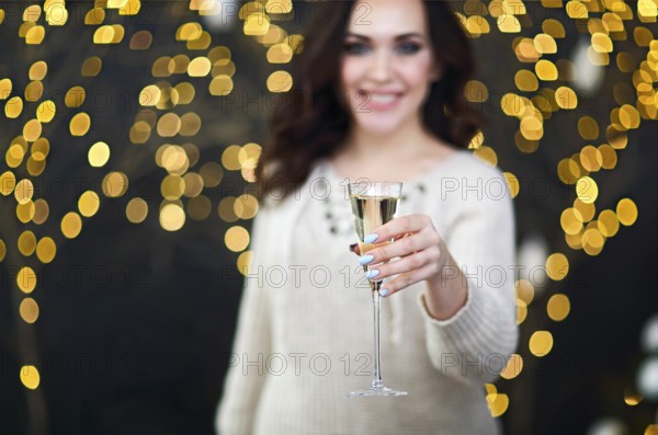 Smiling woman in the sweater with glass of champagne over lights background. Party, drinks, holidays, luxury, friendship and celebration concept