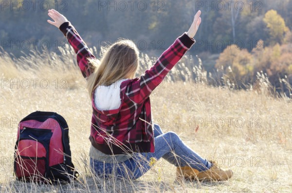 Young happy woman having fun outdoors sitting on the top of the hill. Backpacking tourism concept
