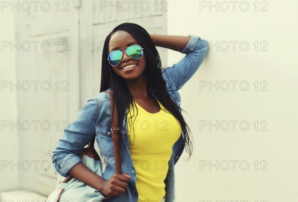 Portrait of happy stylish young african woman in casual clothing, glasses with dreadlocks, backpack posing in the city