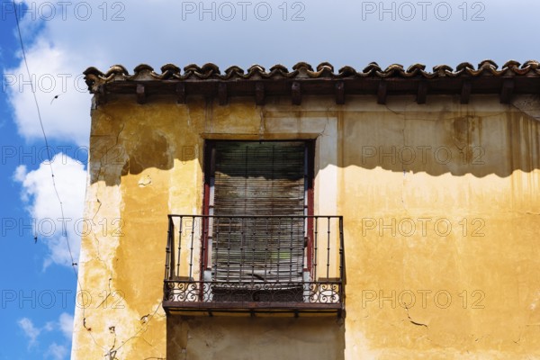 Old Iron Balcony in Aged Yellow Plaster Facade. Old abandoned house