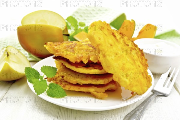 Pumpkin and apple fritters in a white plate, sour cream in a bowl, napkin, mint and fork on wooden board background