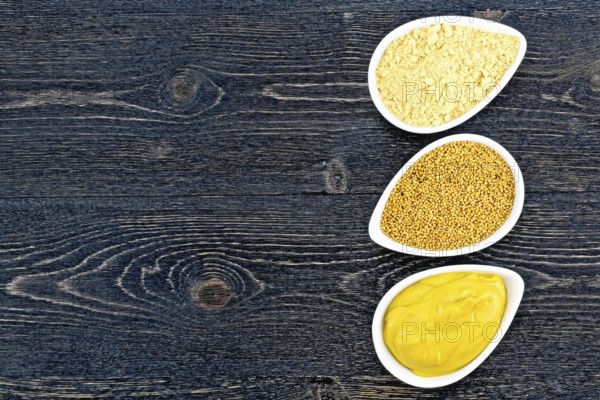 Mustard sauce, seeds and mustard powder in three saucepans on the background of a black wooden board from above
