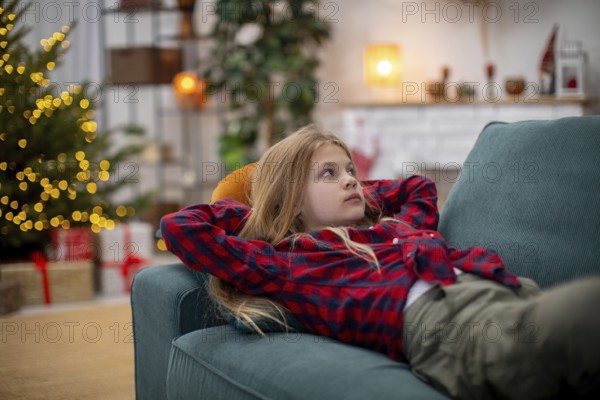 A young child lounges comfortably on a plush sofa, thoroughly enjoying the warm and cozy atmosphere of Christmas