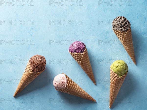 Various ice cream scoops in cones with copy space. Colorful ice cream in cones chocolate, strawberry, blueberry, pistachio or matcha, biscuits chocolate sandwich cookies on blue background. Top view
