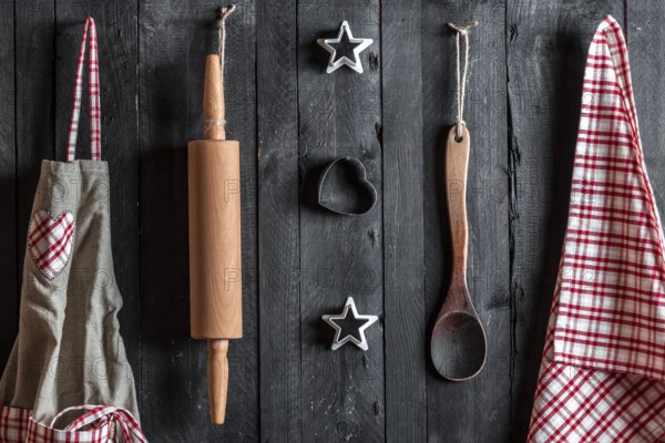 Apron and other kitchen tools hanged with nails on a black wooden wall