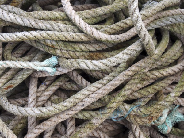 Old worn brown coiled and knotted marine fishing rope with frayed ends stained by the sea