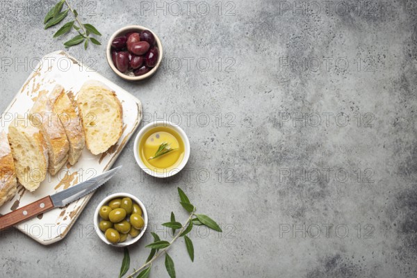 Sliced fresh ciabatta on cutting kitchen board, green and brown olives, olive oil with rosemary, olive tree branches on gray concrete stone rustic background from above copy space, food photography, food photography