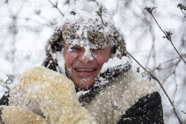 A frozen man covered in winter snow smiles and looks at the camera. The first snow has fallen. A man in a fur hat in cold weather