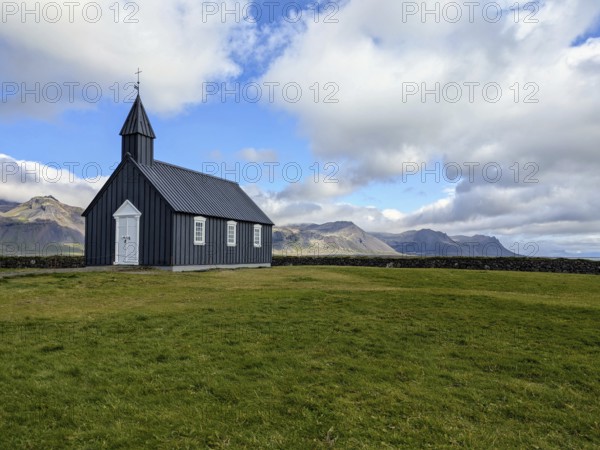 Isolated black church on grassland with mountains in the background under a cloudy sky. Iceland