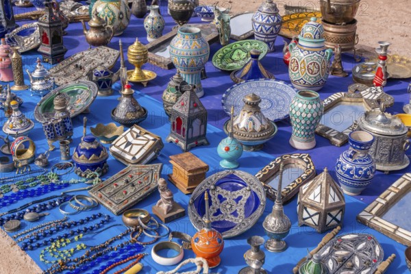 A colorful Moroccan market scene along a bustling street, with vendors selling spices, textiles, and handcrafted goods