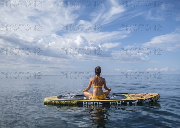Woman practicing yoga on a surfboard under a dramatic sky, Estalella, coast of Llucmajor, Majorca, Balearic Islands, Spain