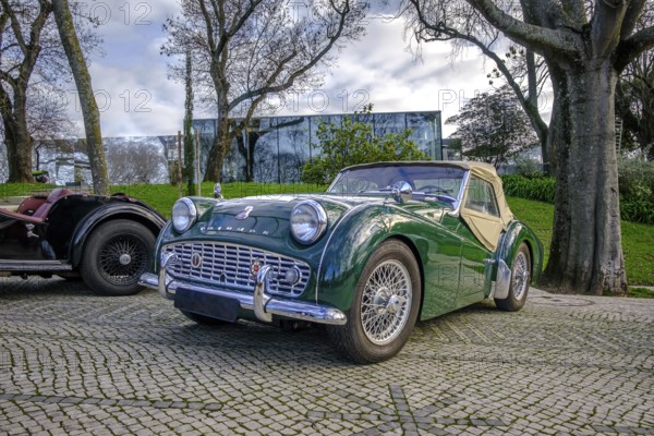 Lisbon, Portugal, Jan 20, 2024: A classic green Triumph TR3A soft top drophead car cobblestone driveways by another vintage vehicle on sunny spring day