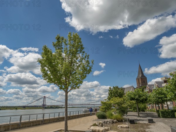 A tree and a church next to a footpath with a river and a bridge in the background, emmerich, lower rhine, germany