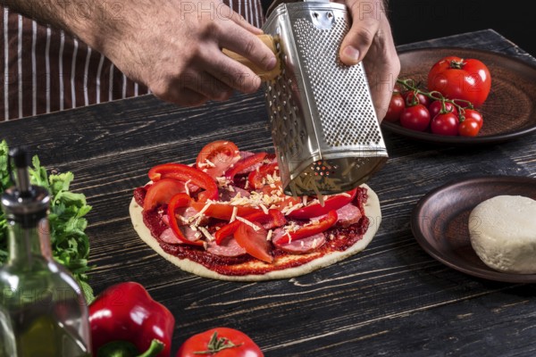 Cook in the kitchen putting the ingredients on the pizza on an old wooden background. Pizza concept. Production and delivery of food. Cooking concept. Close-up