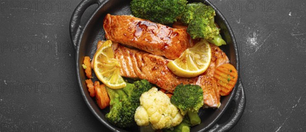Healthy baked fish salmon steaks, broccoli, cauliflower, carrot in cast iron casserole bowl black dark stone background. Cooking a delicious low carb dinner, healthy nutrition, food photography