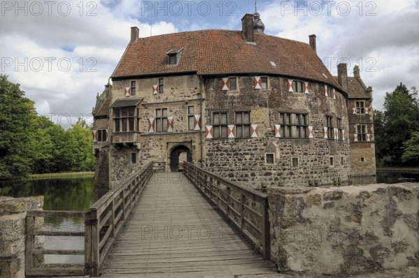 Wide bridge leads to a historic castle with moat, surrounded by nature, cloudy sky, lüdinghausen, münsterland, germany